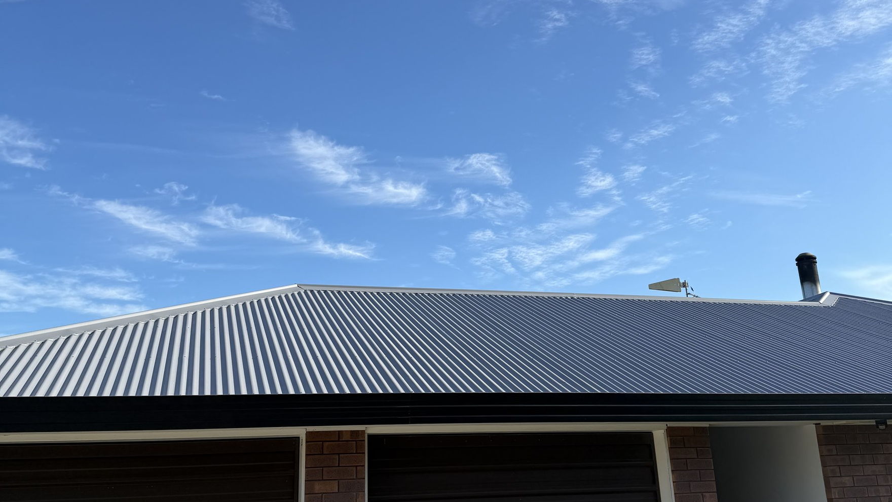Freshly painted light grey corrugated iron roof against a blue sky