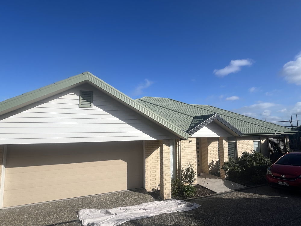 Single storey Christchurch house with the roof painted sage green and drop sheets over the driveway