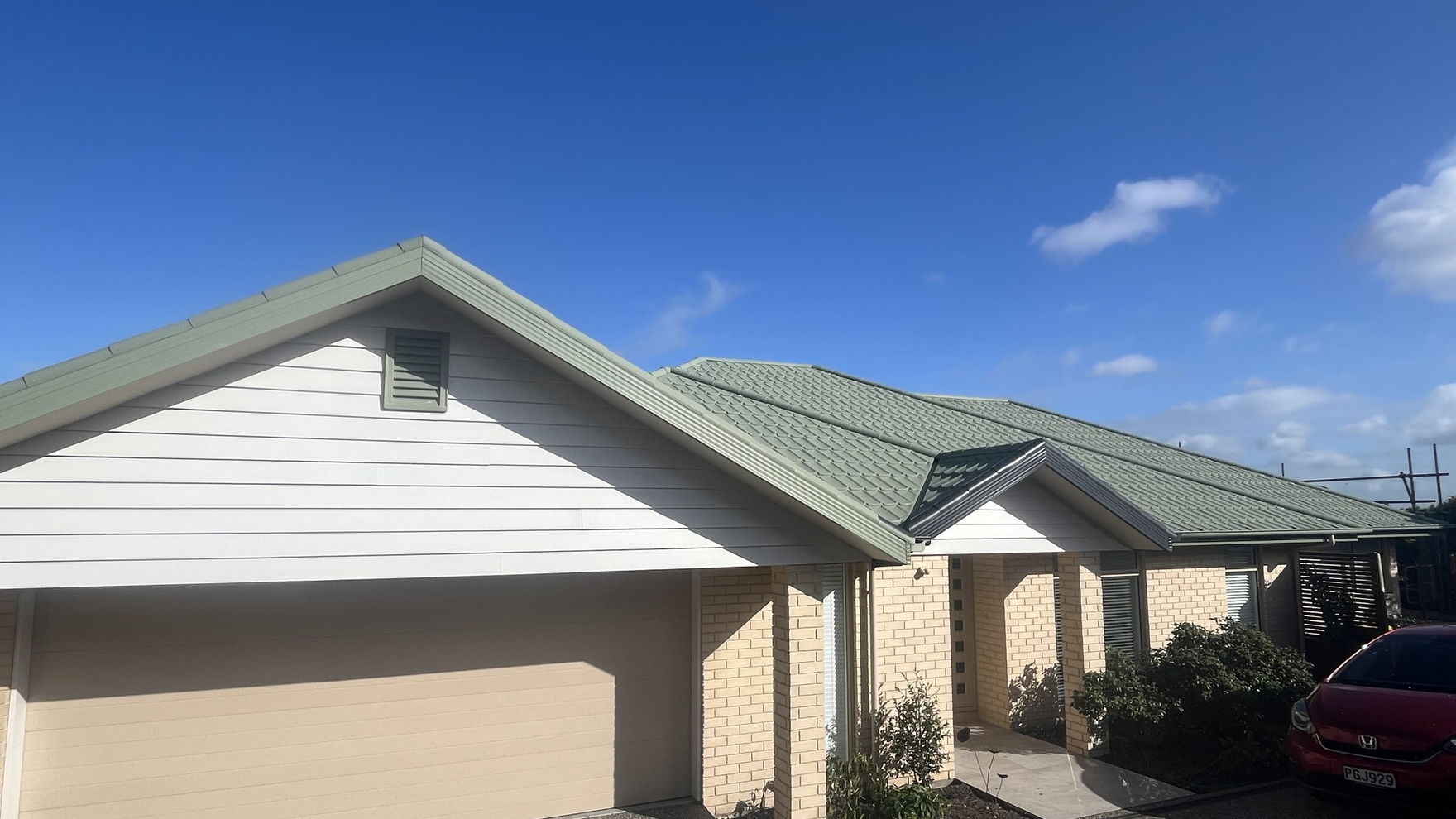 Roof painting in progress on a Christchurch house, the roof in sage green and drop sheets protecting the driveway