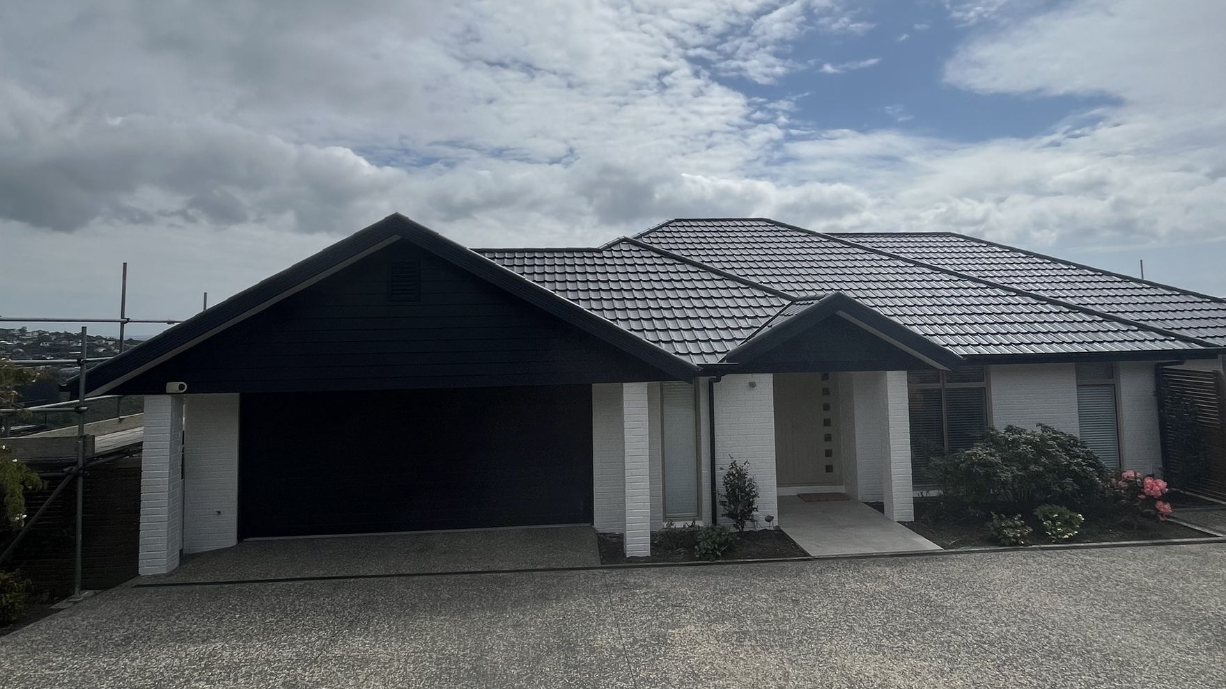 Christchurch home with a freshly painted dark grey concrete tile roof over white brick and a black garage door
