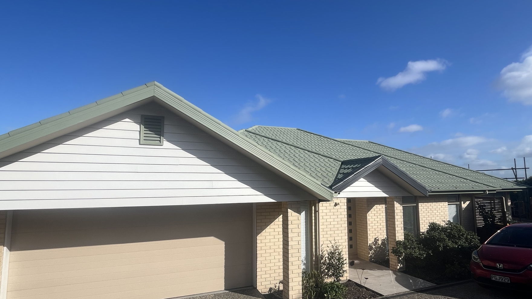 Single storey Christchurch house with its roof painted sage green, drop sheets laid over the driveway below