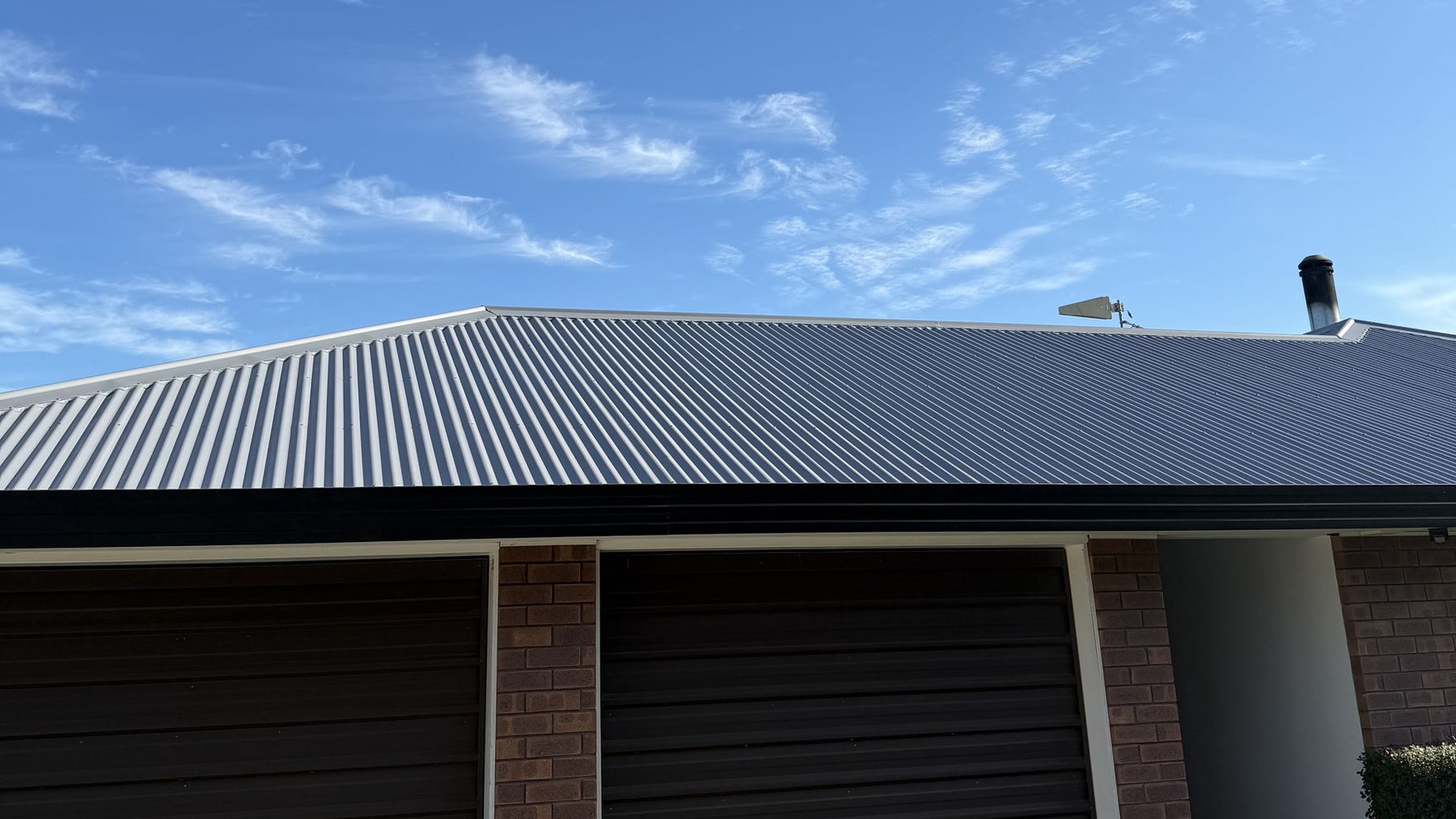 Light grey corrugated iron hip roof over a brick garage near Lincoln, freshly painted under a blue sky